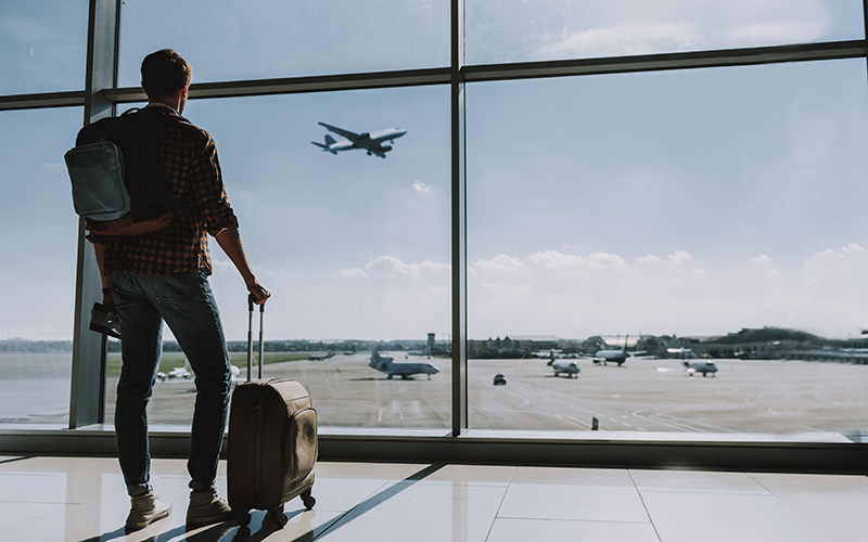 Mann steht am Flughafen und schaut in Richtung eines Flugzeugs